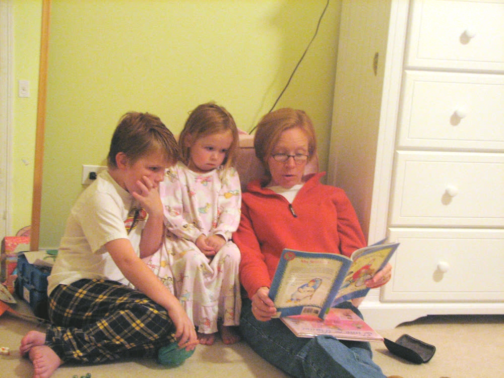 A woman reading a picture book aloud to two children beside her